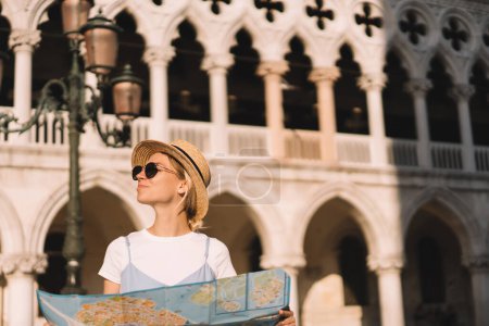 Attractive woman in sunglasses holding paper map for choosing adventure direction during recreation vacations in Venezia, beautiful Caucasian tourist exploring showplaces of romantic Italian city