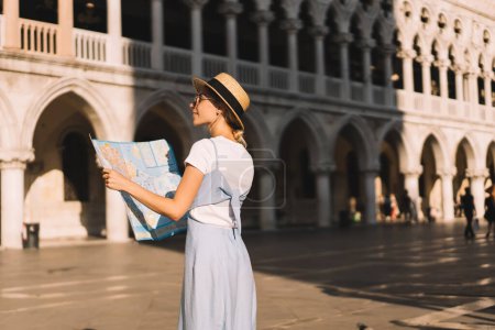 Touristic female wanderer enjoying Italian romantic vacations for exploring summer Venezia city during solo getaway journey, Caucasian woman with navigation map looking around San Marco Square