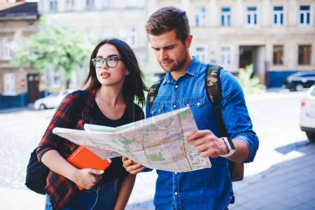 Photo for Caucasian male and female friends travelers enjoying trip on vacation strolling with map on sightseeing tour, couple in love in casual wear searching direction for notable city places together - Royalty Free Image