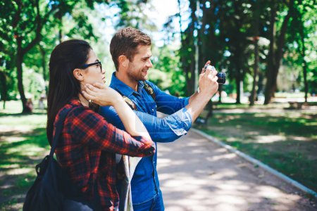 Photo for Positive caucasian man photographier enjoying spending free time on hobby making photos in park with girlfriend, couple of tourists using camera focusing on locations while visiting town on weekend - Royalty Free Image