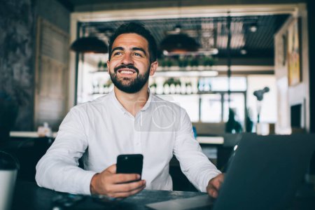 Cheerful caucasian businessman satisfied with earning online money getting transaction sitting in coffee shop with technology, happy prosperous male freelancer use modern devices for remote job