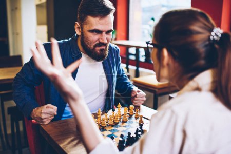 Cultivo hombre enojado en ropa casual en conflicto con la mujer irreconocible disgustado mientras juega al ajedrez como complicada relación seria de pareja durante la crisis