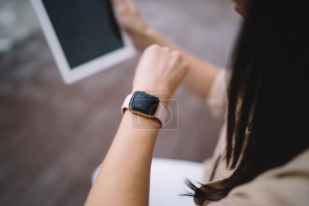 Cropped image of millennial female checking received notification on mockup smartwatch with copy space touchscreen for application advertising, selective focus on wearable gadget with blank display