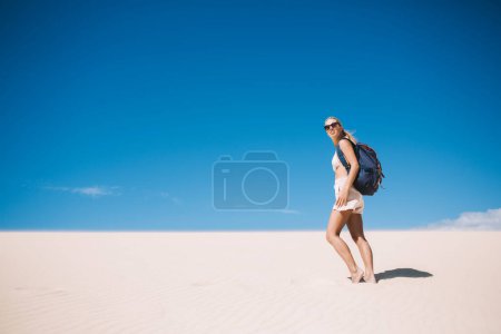 Femme blanche errant dans des lunettes de soleil à la mode explorant l'environnement des dunes arides pendant les vacances de voyage pour les loisirs d'été, jeune femme avec sac à dos touristique visitant la vallée de la mort africaine