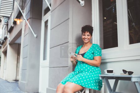 Porträt einer fröhlichen Millennial-Bloggerin in grünem Kleid mit Tupfen, die internationale Internetverbindung in der Freizeit auf einem modernen Mobiltelefon nutzt, Konzept der Technologie
