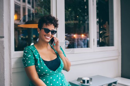 Porträt des hispanischen Models Xl mit stylischer Sonnenbrille, die während der Freizeit Handy-Gespräche für die internationale Kommunikation genießt, glückliche, zahme Frau, die sich mit 4g drahtlosem Internet zum Telefonieren verbindet