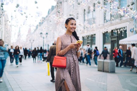 Téléchargez les photos : Heureuse femme asiatique avec la technologie numérique smartphone à la main se promener dans la ville touristique profiter des vacances d'été pour voyager, joyeuse fille millénaire avec téléphone portable explorer une nouvelle rue - en image libre de droit