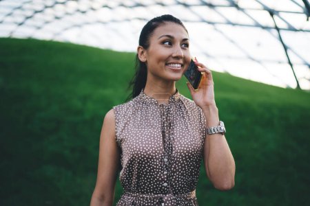 Foto de Mujer asiática alegre utilizando la conexión celular para hacer conversación en línea durante el tiempo libre en invernadero verdor, próspera mujer milenaria comunicarse con amigo a través de la aplicación de movilidad - Imagen libre de derechos