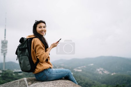 Foto de Retrato de mujer viajera asiática sonriente descansando durante las vacaciones de viaje explorar lugares y lugares históricos, mujer alegre turista con mochila y teléfono inteligente satisfecho con la conexión - Imagen libre de derechos