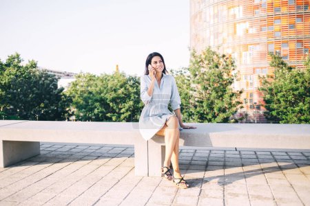 Schöne kaukasische Frau in Freizeitkleidung sitzt im städtischen Umfeld Hintergrund mit Handy-Gespräch, attraktive 20er Jahre Hipster-Mädchen Reisende mit Roaming-Verbindung zum Telefonieren im Freien