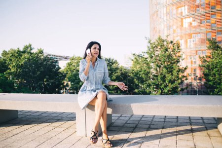 Positive weibliche Gespräche auf dem Handy während der Freizeit im Freien mit guter Roaming-Verbindung und Tarifen, lächelnde Reisende genießen sonnige Tage in der Innenstadt mit Smartphone-Gesprächen