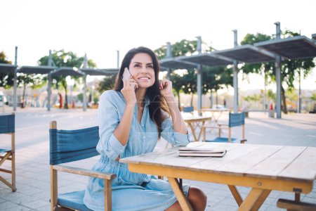 Schöne positive Frau in Freizeitkleidung, die sich auf der Caféterrasse ausruht und Handy-Gespräche genießt, Millennials der 30er Jahre, die auf dem Smartphone im Roaming mit der Verbindung auf der Straße zufrieden sind