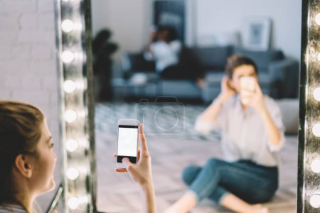 Blogger de influencia caucásica recortada utilizando la aplicación en el gadget de teléfono inteligente maqueta para hacer imágenes espejo durante el tiempo libre en el apartamento en casa, chica milenaria creando contenido celular de medios
