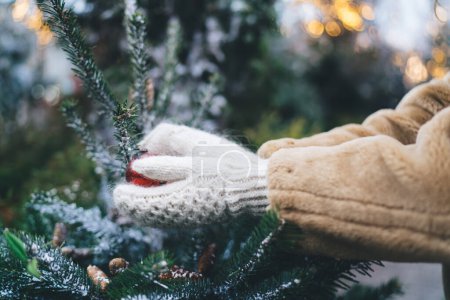 Téléchargez les photos : Vue latérale de la culture femme anonyme en manteau chaud et gants tenant boule de sapin de Noël dans les mains pendant les vacances d'hiver - en image libre de droit