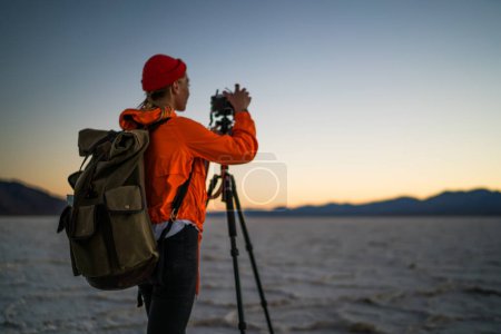Back view of from below anonymous female photographer checking photos after shooting landscape in desert while traveling around Badwater Basin in USA