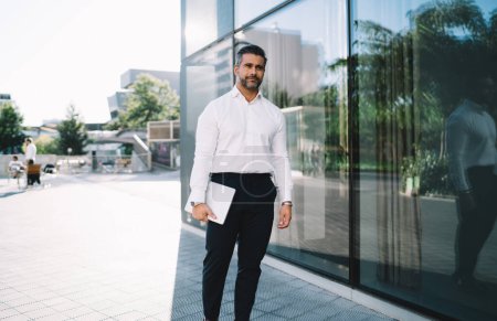 Umsichtiger Geschäftsmann im weißen Hemd mit digitaler Laptop-Technologie, der nachdenklich wegschaut und über Marktidee nachdenkt, gelernter Unternehmer in formaler Kleidung, der über Netbook-Projektion nachdenkt