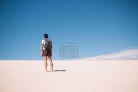 Vue arrière de jeune touriste debout au sable de la vallée de la mort et regardant autour de dunas sauvages, vagabond mâle avec sac à dos passer des vacances d'été pour visiter safari inhabité au Maroc