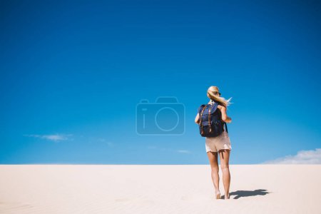 Vue arrière de la femelle avec sac à dos explorant les terres arides du désert en vacances d'été dans un point de repère de la nature, femme errant avec sac à dos dans le parc national des sables blancs près des dunes venant à l'horizon