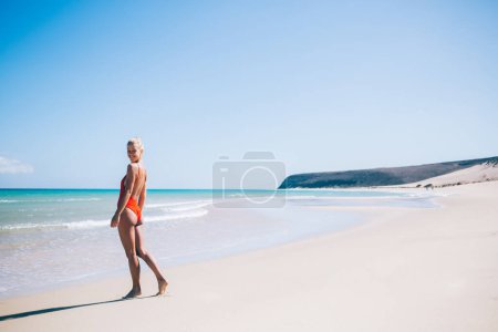 Téléchargez les photos : Portrait complet d'une touriste féminine gaie posant sur une plage de sable explorant le littoral des Seychelles, heureuse voyageuse en maillot de bain élégant bronzant pendant les vacances récréatives à Minorque - en image libre de droit