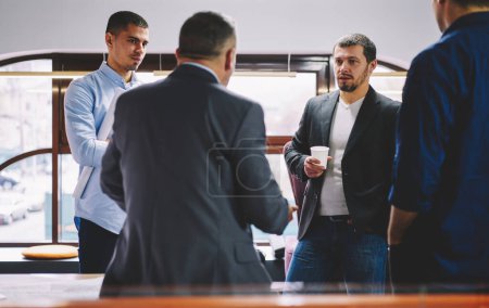Professional male colleagues have business conversation during brainstorming in company office, crew of executive managers in smart casual wear communicating about involved project and analytics