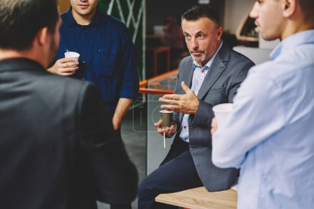 Los colegas masculinos profesionales tienen conversación de negocios durante el descanso del café en la oficina de la compañía, equipo de gerentes ejecutivos en ropa casual inteligente que se comunican sobre el proyecto involucrado y la analítica