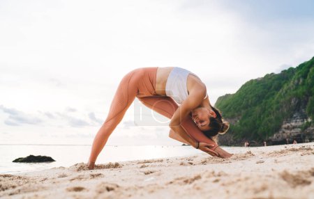 Foto de Cuerpo completo de mujer elegante haciendo pirámide con las manos en el interior del ejercicio de la pierna durante la sesión de yoga al aire libre - Imagen libre de derechos