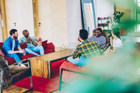 Eine multiethnische Gruppe von Hipstern sitzt mit Kaffee auf einer bequemen Couch in einer modernen Wohnung und kommuniziert, männliche und weibliche Freunde diskutieren etwaige gemeinsame Zeit zu Hause