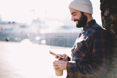 Junger Hipster-Typ, der während seiner Freizeit in der Stadt Smartphone-Mobilitätsnetzwerke mit 4g Wireless für die Verbindung genießt, Millennial-türkischer Blogger mit mobiler Webveröffentlichung in den sozialen Medien