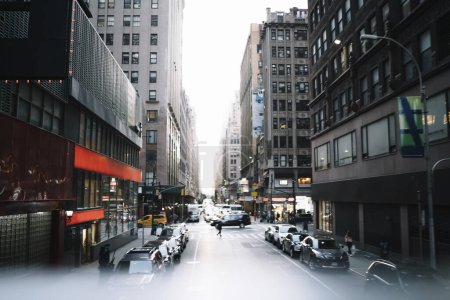 Foto de Perspectiva de la calle de la ciudad con coches aparcados a lo largo de las aceras con gente caminando bajo rascacielos altos en un día tranquilo en la ciudad de Nueva York - Imagen libre de derechos