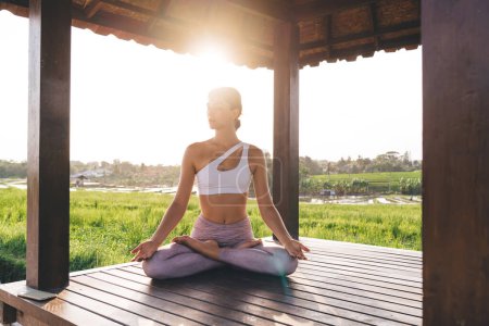 Calm female in sportswear praying and meditating during holistic healing at leisure, Caucasian woman enjoying time for appeasement and enlightenment mindfulness during yoga practice near rice fields