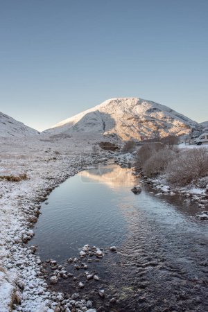 Foto de El río Coe en Glencoe se extiende hacia montañas cubiertas de nieve bajo un cielo azul claro. Scottish Highlands, Reino Unido - Imagen libre de derechos