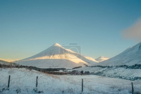 Beinn Dorain, una montaña cónica, cubierta de nieve bajo un cielo azul, a lo largo del West Highland Way en Escocia