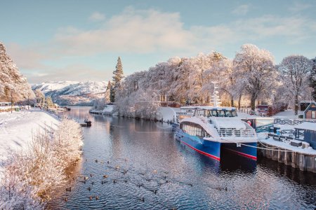 Photo for Loch Ness cruise boats on the Caledonian Canal in Fort Augustus with snow-covered surroundings, on a sunny winter day - Royalty Free Image