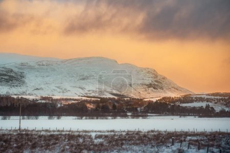 A snow-covered mountain landscape at sunset in Laggan, Scotland