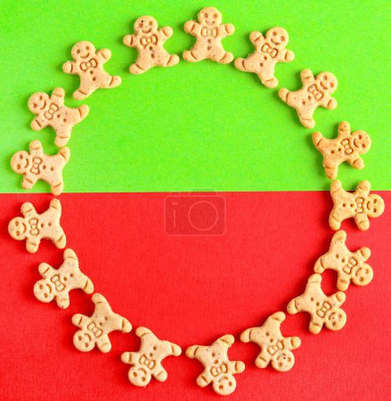 Foto de Mini galletas de jengibre hombres en forma de círculo sobre fondo verde y rojo. Patrón de símbolos de Navidad en verde y rojo - Imagen libre de derechos