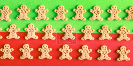 Téléchargez les photos : Mini pain d'épice hommes biscuits sur fond vert et rouge. Modèle de symboles de Noël sur vert et rouge - en image libre de droit
