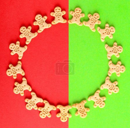 Téléchargez les photos : Mini pain d'épice hommes biscuits en forme de cercle sur fond vert et rouge. Modèle de symboles de Noël sur vert et rouge - en image libre de droit