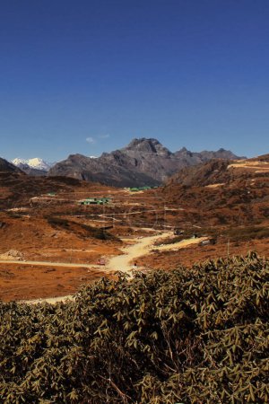 Foto de Camino de tierra de montaña zigzag pasando por el hermoso valle alpino y la remota zona rural de Tawang, rodeado de montañas himalaya nevadas - Imagen libre de derechos