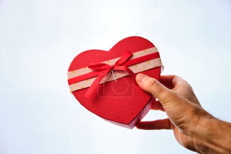 Téléchargez les photos : Man's hand giving a gift in the shape of a heart on a white background. Valentine's Day. - en image libre de droit