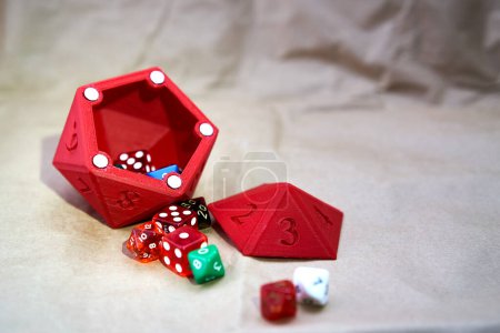 Photo for Several dice of different sizes and colors, with a red dice cup in the shape of a die on a cardboard-like surface. - Royalty Free Image