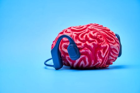 Rotes Gummihirn mit Kopfhörern auf blauer Oberfläche. Konzept der Gehirnruhe.
