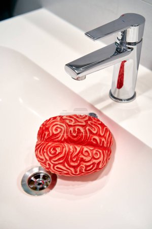 Photo for Red Rubber Human Brain under a Sink Faucet, Brainwashing Concept. - Royalty Free Image