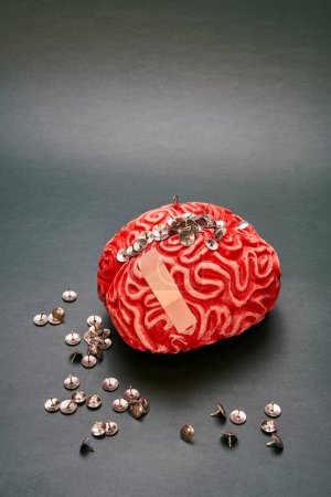 Nahaufnahme eines menschlichen Gehirns aus rotem Gummi mit einem Bündel von Daumenknöpfen darauf vor dunklem Hintergrund. Konzept der extremen Kopfschmerzen.