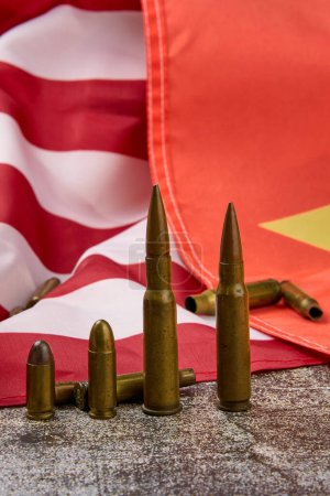 Groupe de balles de différents calibres alignées avec les drapeaux américain et chinois en arrière-plan.