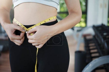 Foto de Mujer joven midiendo su cintura por cinta métrica en el gimnasio. - Imagen libre de derechos