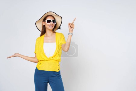 Foto de Mujer de raza mixta feliz usando un sombrero de sol y gafas de sol, apuntando a espacio de copia vacío aislado sobre fondo blanco. - Imagen libre de derechos