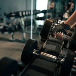 Close-up woman hands lifting dumbbells at gym.
