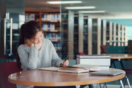 Junge asiatische Studentin macht Nackenmassage und entspannt sich an ihrem Tisch in der Bibliothek.