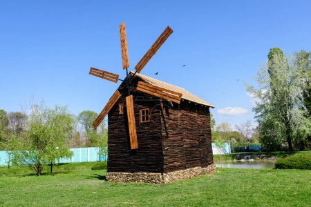 Decorative old wood mill and green grass on a small island on the lake from the Chindiei Park (Parcul Chindiei) in Targoviste, Romania, in a sunny spring day