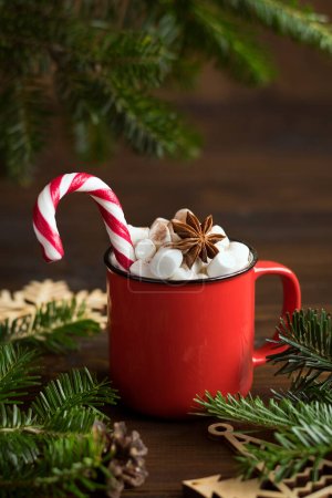 Bebida de Navidad. Cacao o chocolate caliente con malvaviscos en una taza roja con un bastón de caramelo, con ramas de abeto en una mesa de madera oscura. Tarjeta de Navidad. Copiar espacio.